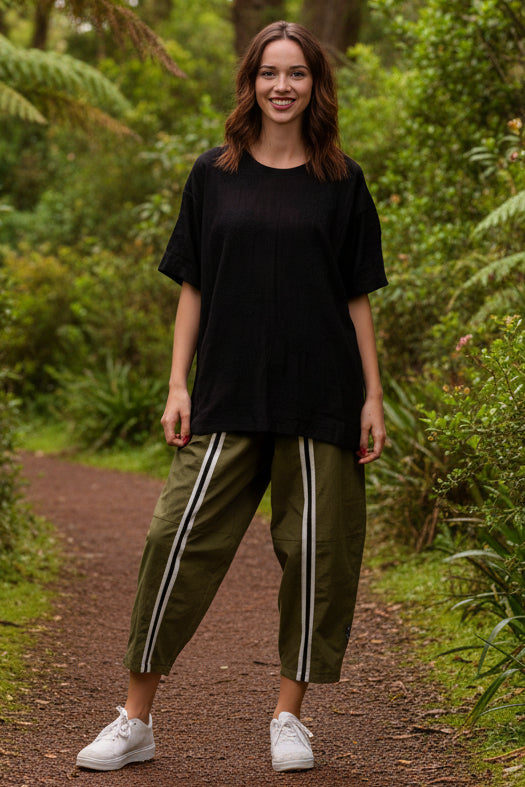 Woman wearing a black oversized top and green pants with white stripes on a white background