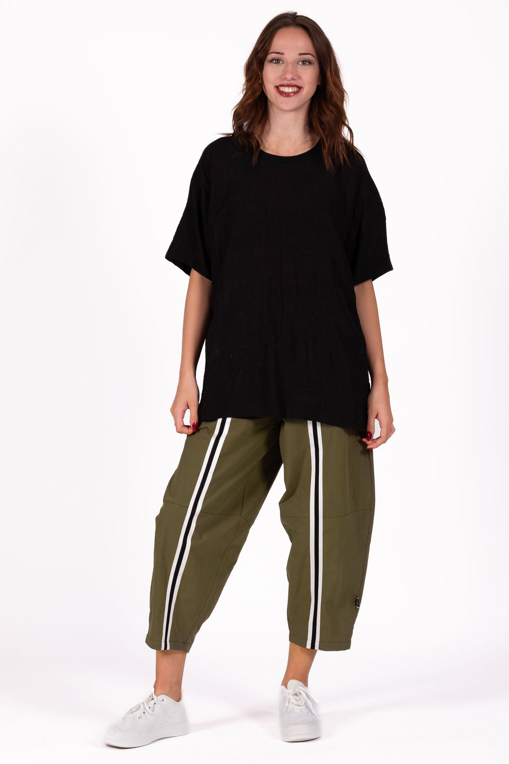 Woman wearing a black oversized top and green pants with white stripes on a white background