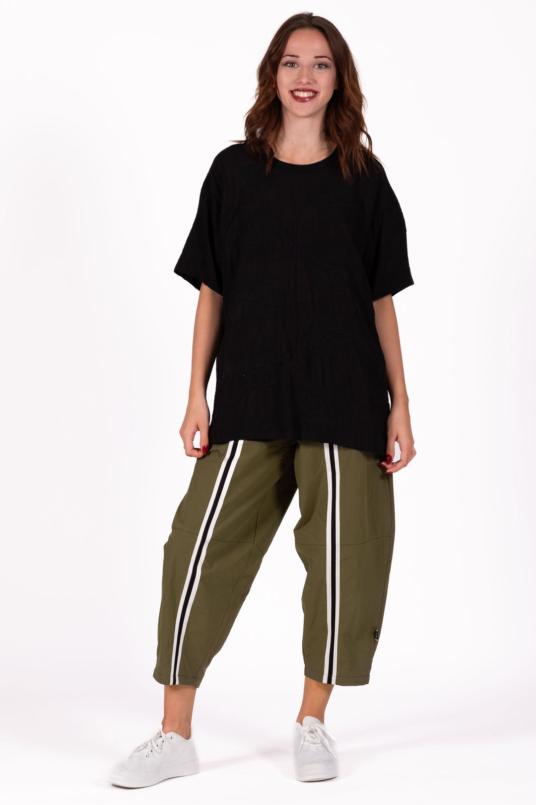 Woman wearing a black oversized top and green pants with white stripes on a white background