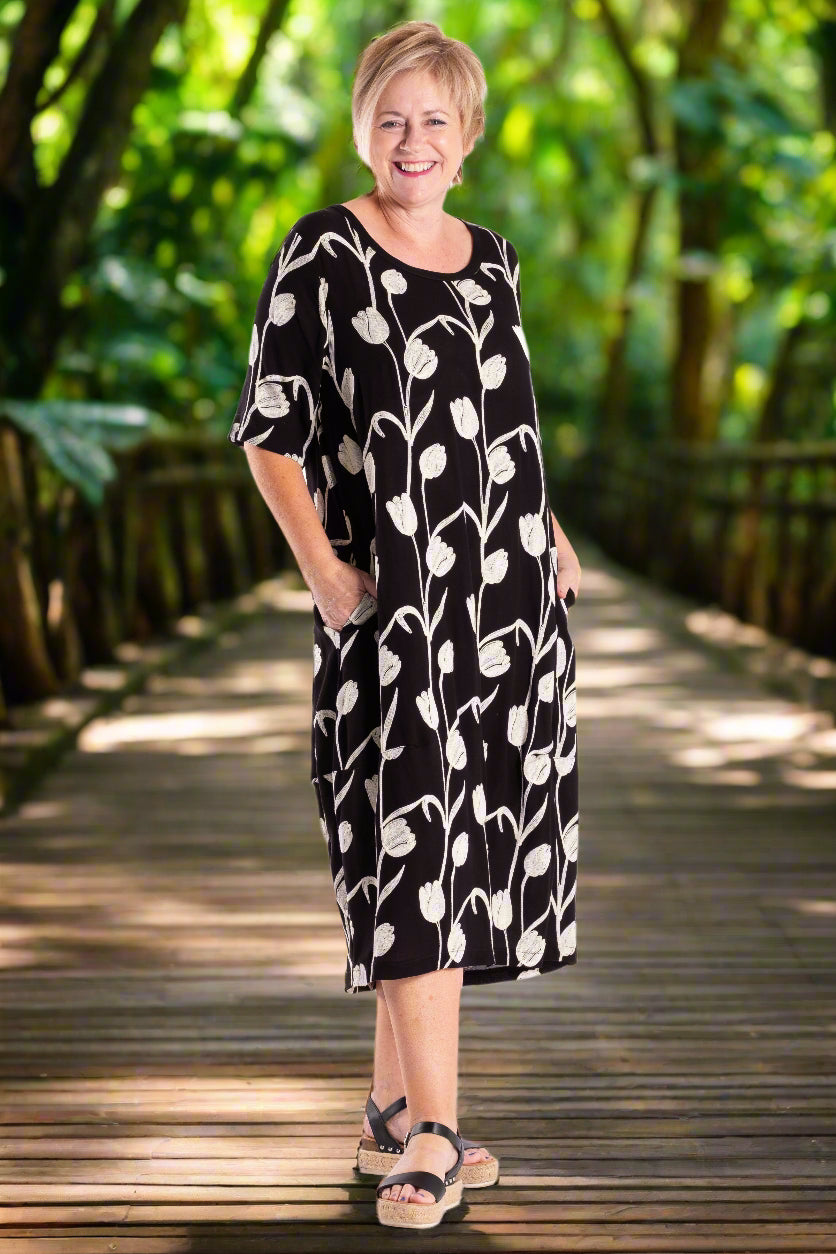 Woman wearing a black deeanne hobbs dress with white floral pattern on a white background