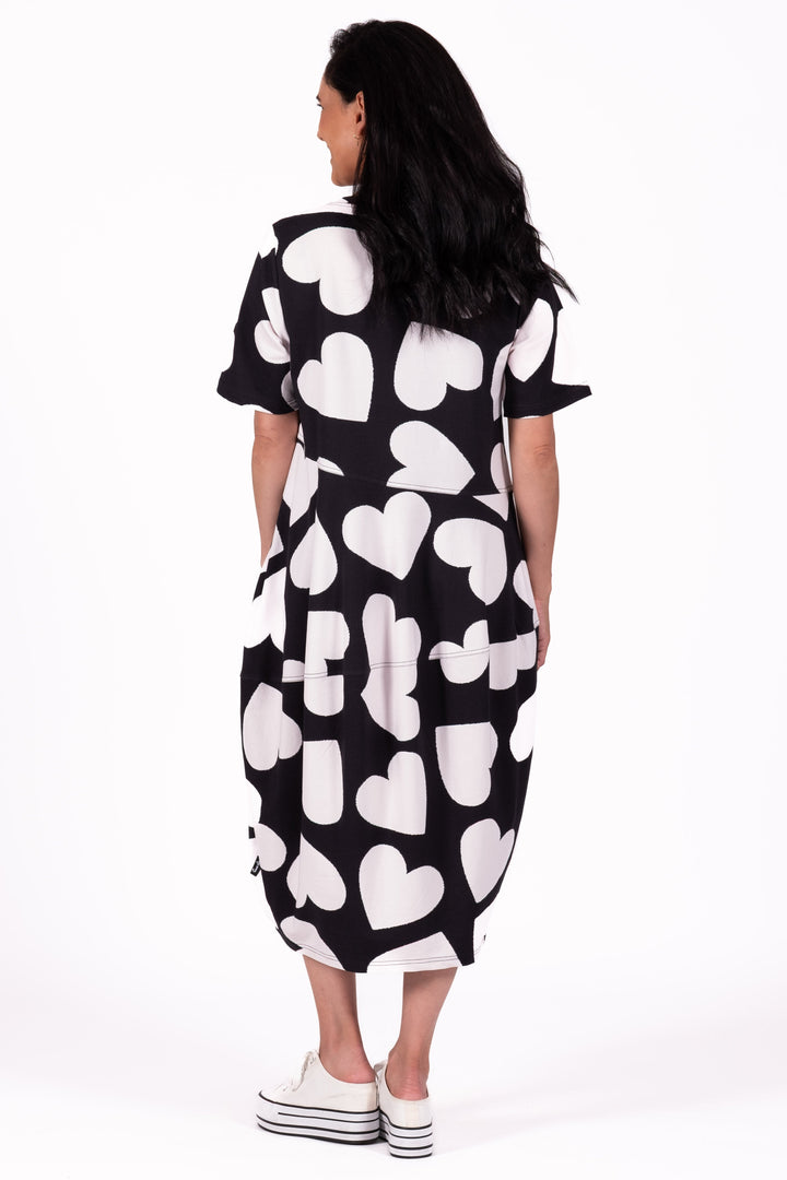 A woman viewed from behind wearing a short-sleeve midi dress with a black and white heart pattern, paired with white platform sneakers, against a plain white studio background.