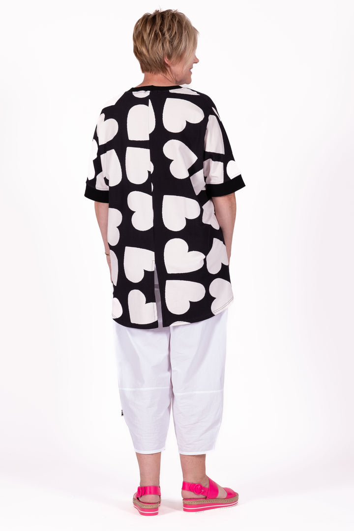 Person wearing a black and white patterned shirt with white pants on a white background