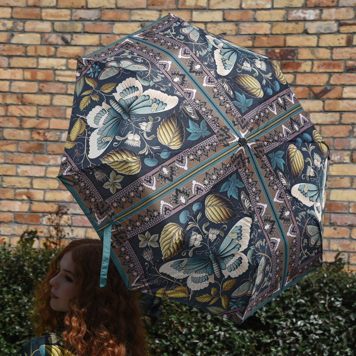 Person holding a decorative umbrella with butterfly pattern against a brick wall.