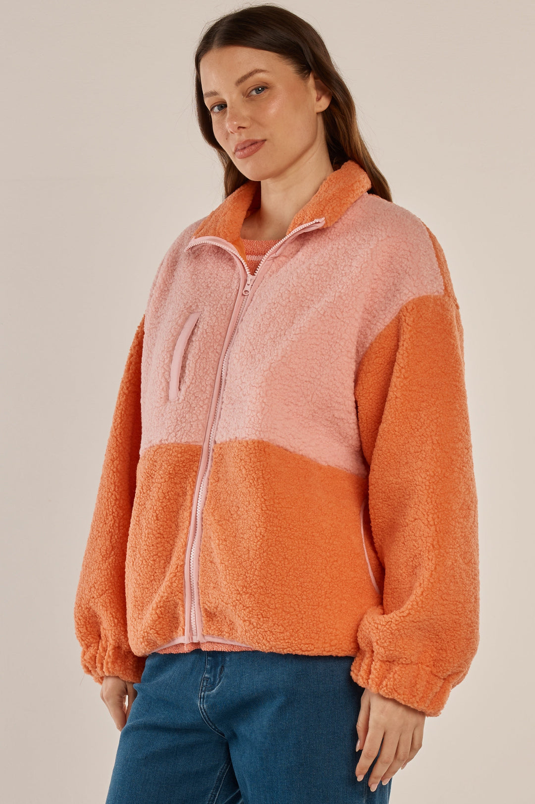 Woman wearing a two-tone pink and orange fleece jacket on a beige background