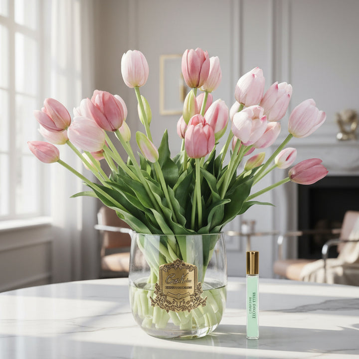 Bouquet of pink cote noire diffuser tulips in a clear vase with a small bottle on a white background