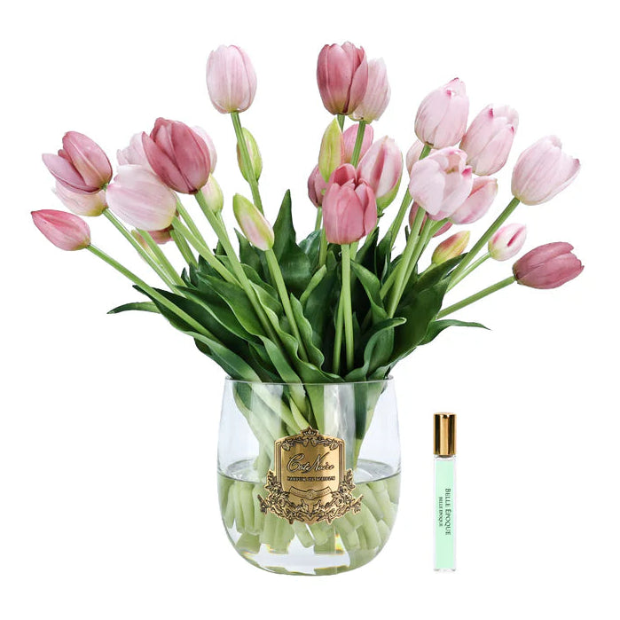 Bouquet of cote noire pink tulips in a clear vase with a perfume bottle on a white background