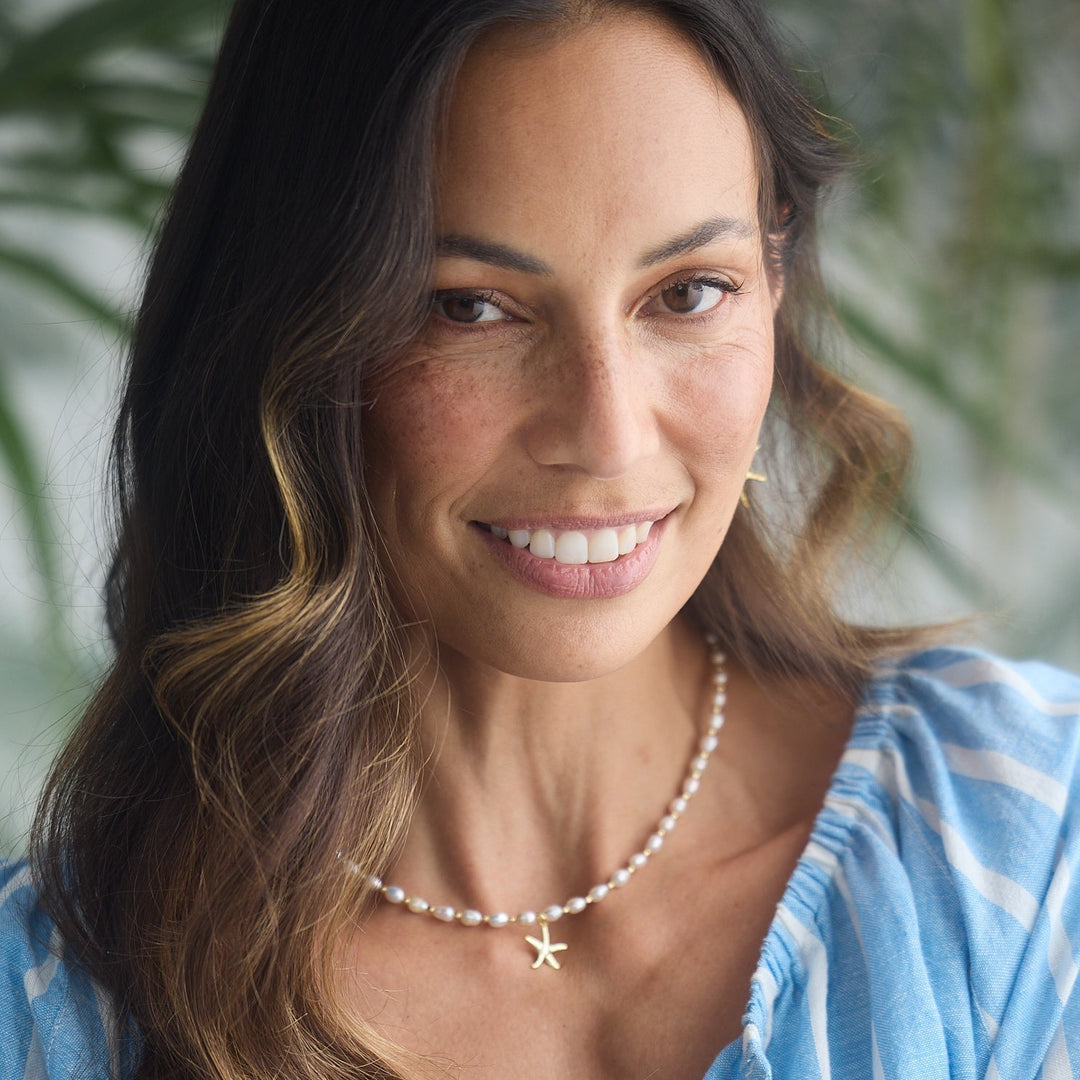 Woman wearing a blue and white striped dress with a blurred green plant background