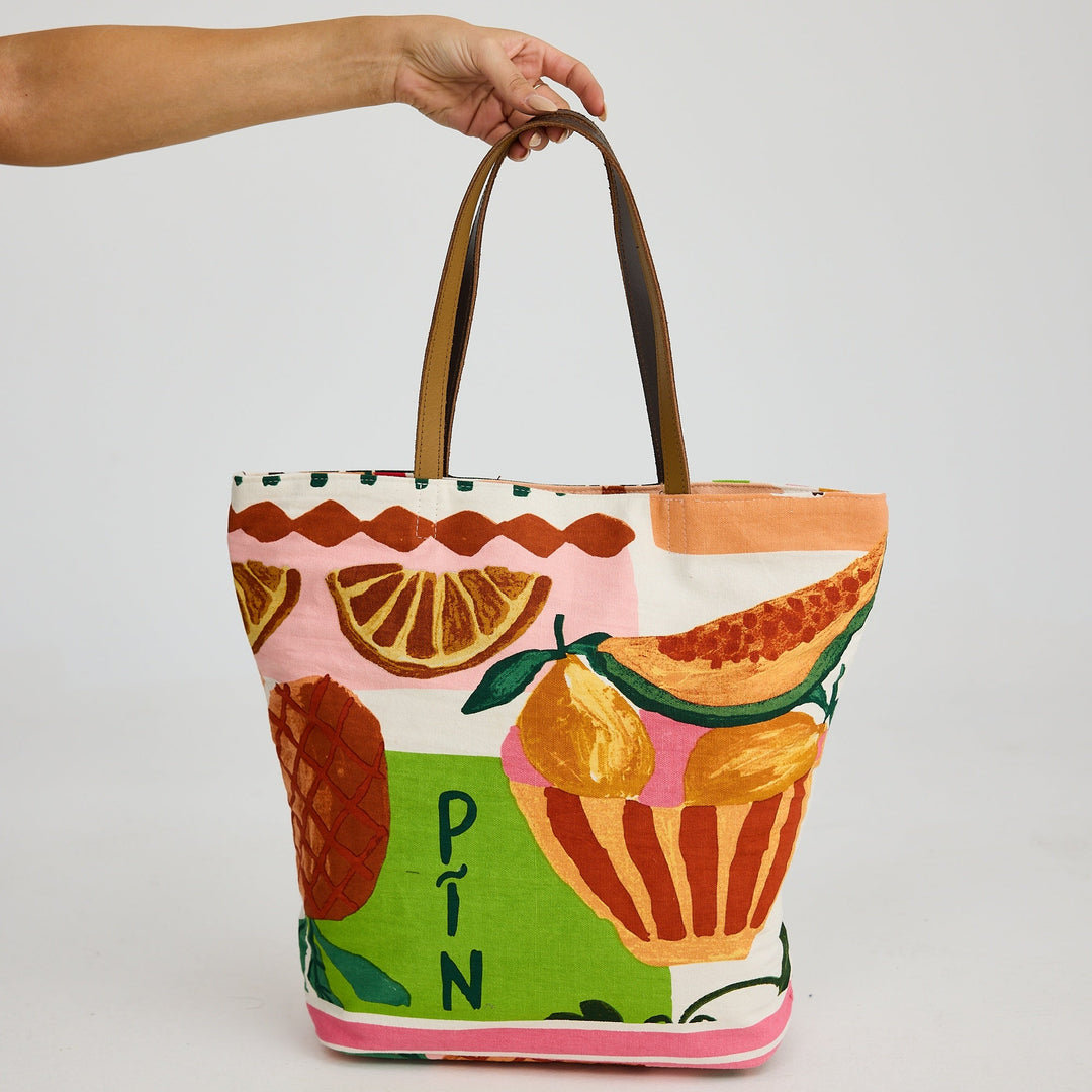 Tote bag with fruit design held by a hand on a light gray background
