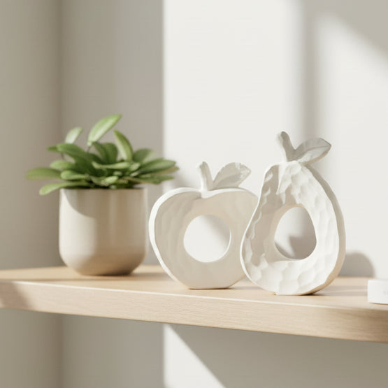 Two white ceramic fruit-shaped wall decor pieces, shaped like a pear and a stylized apple, displayed on a clean white background.
