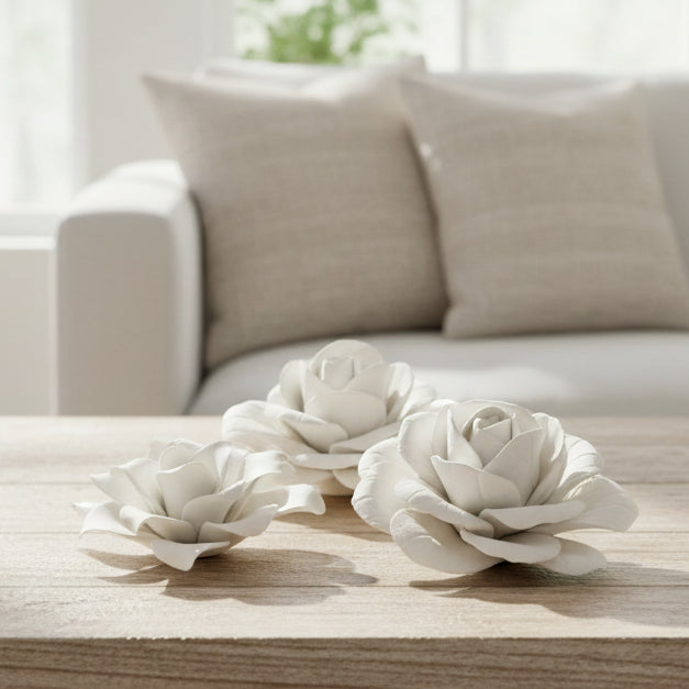Three sculptural white artificial flowers, including two roses and one peony, arranged on a light gray background.