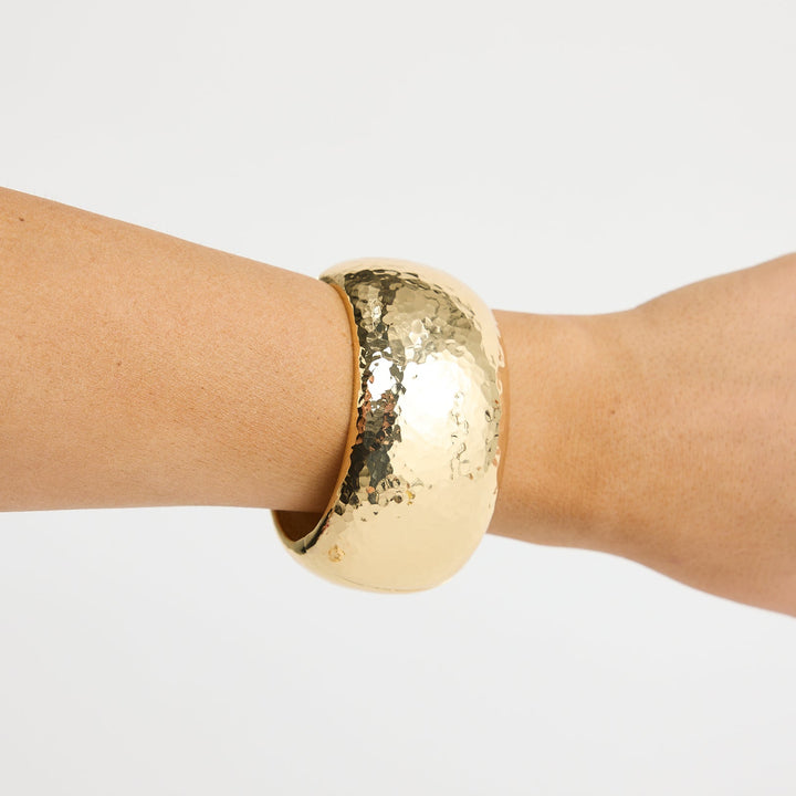 Gold bracelet on a wrist against a white background