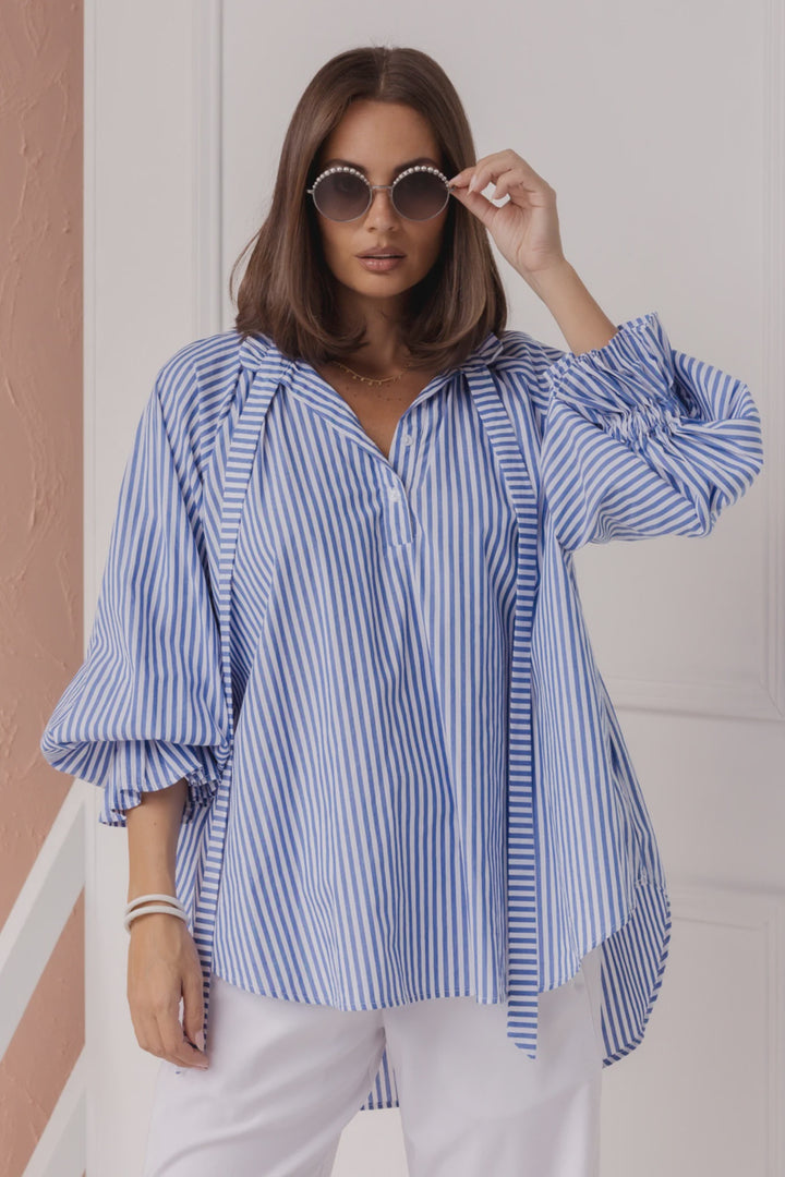Woman wearing a blue and white striped shirt with white pants indoors.
