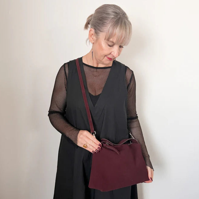 Woman holding a burgundy handbag against a plain background