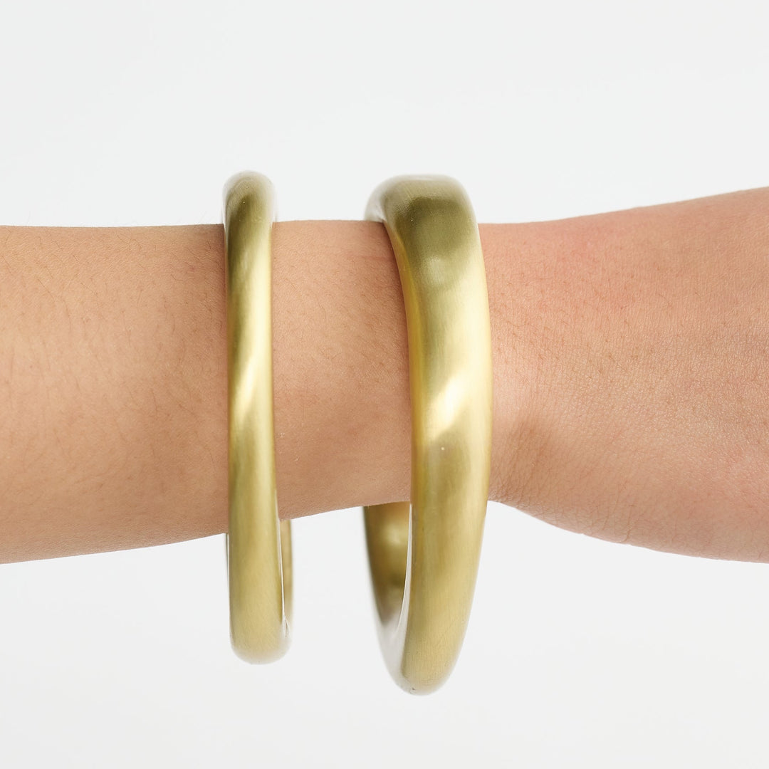 Gold bangles on a wrist against a white background