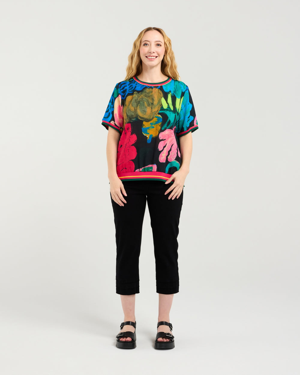 Woman wearing a colorful patterned top and black pants on a white background