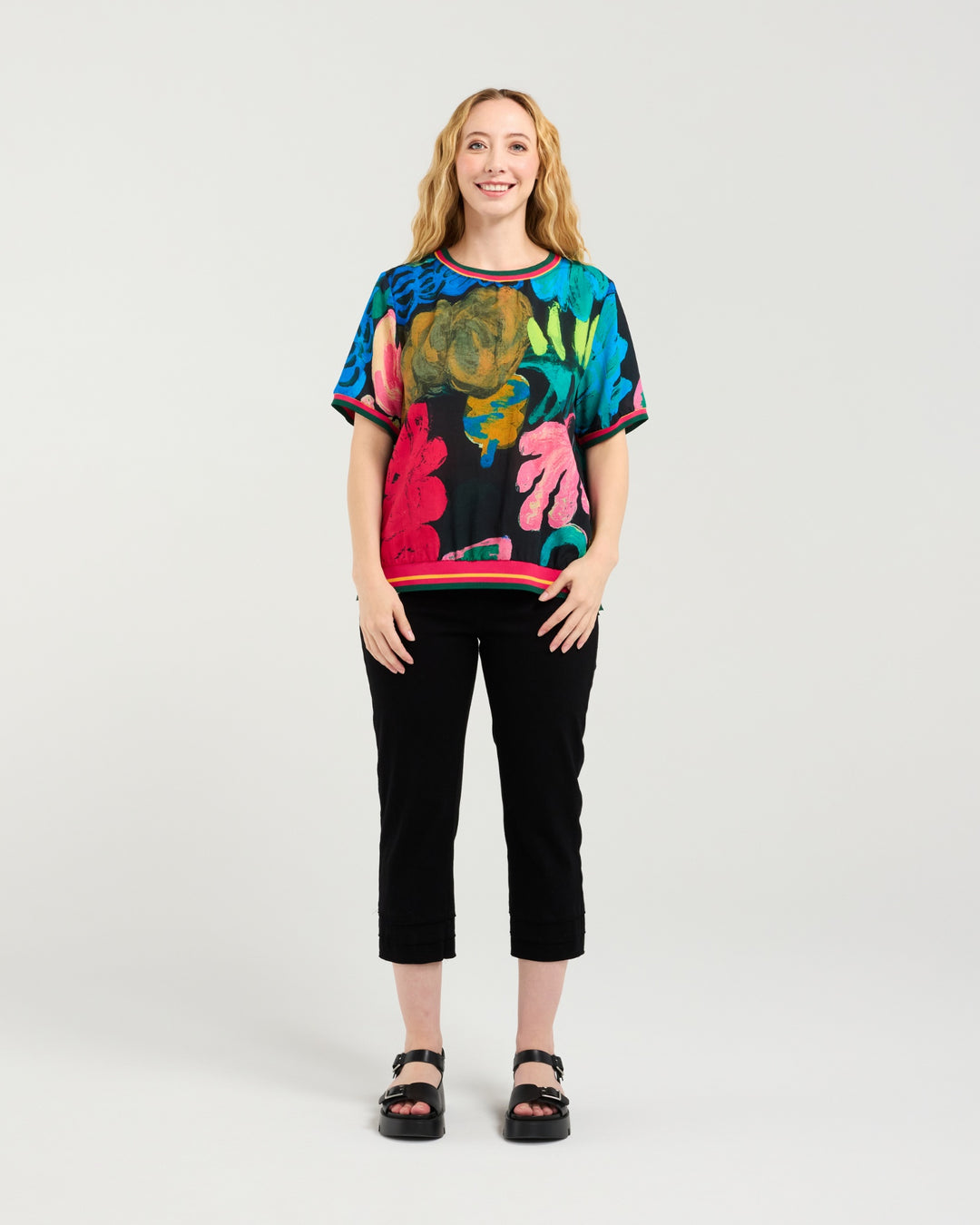Woman wearing a colorful patterned top and black pants on a white background