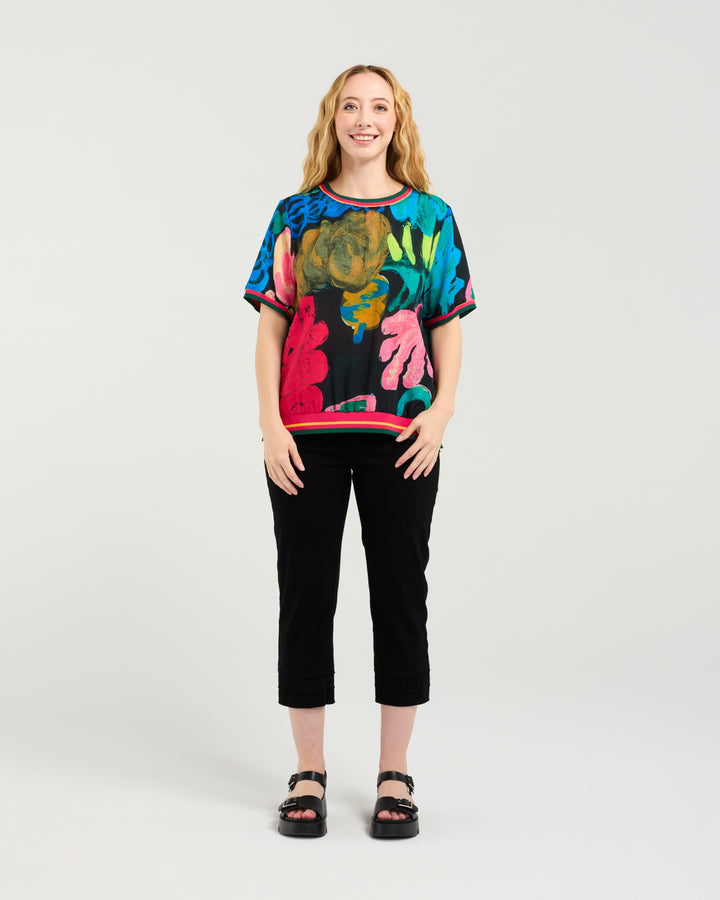 Woman wearing a colorful patterned top and black pants on a white background