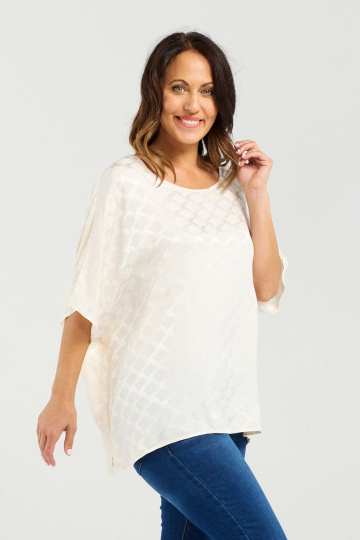 Woman wearing a white poncho and blue jeans on a plain background