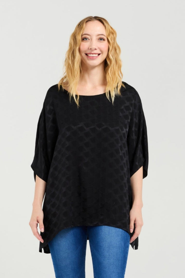 Woman wearing a black patterned top and blue jeans on a white background