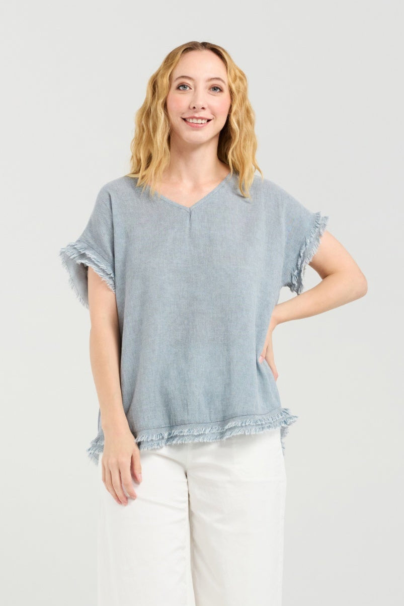 Woman wearing a light blue top and white pants on a plain background