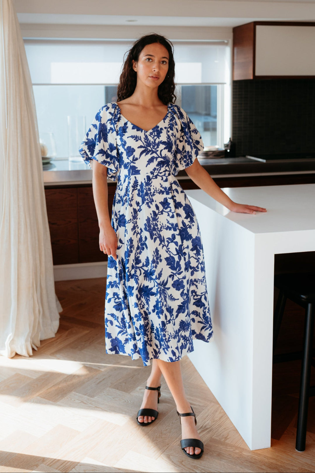 Woman in a blue floral dress standing in a modern kitchen.