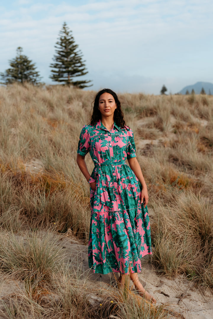 Woman in a patterned dress standing in a field with trees and mountains in the background