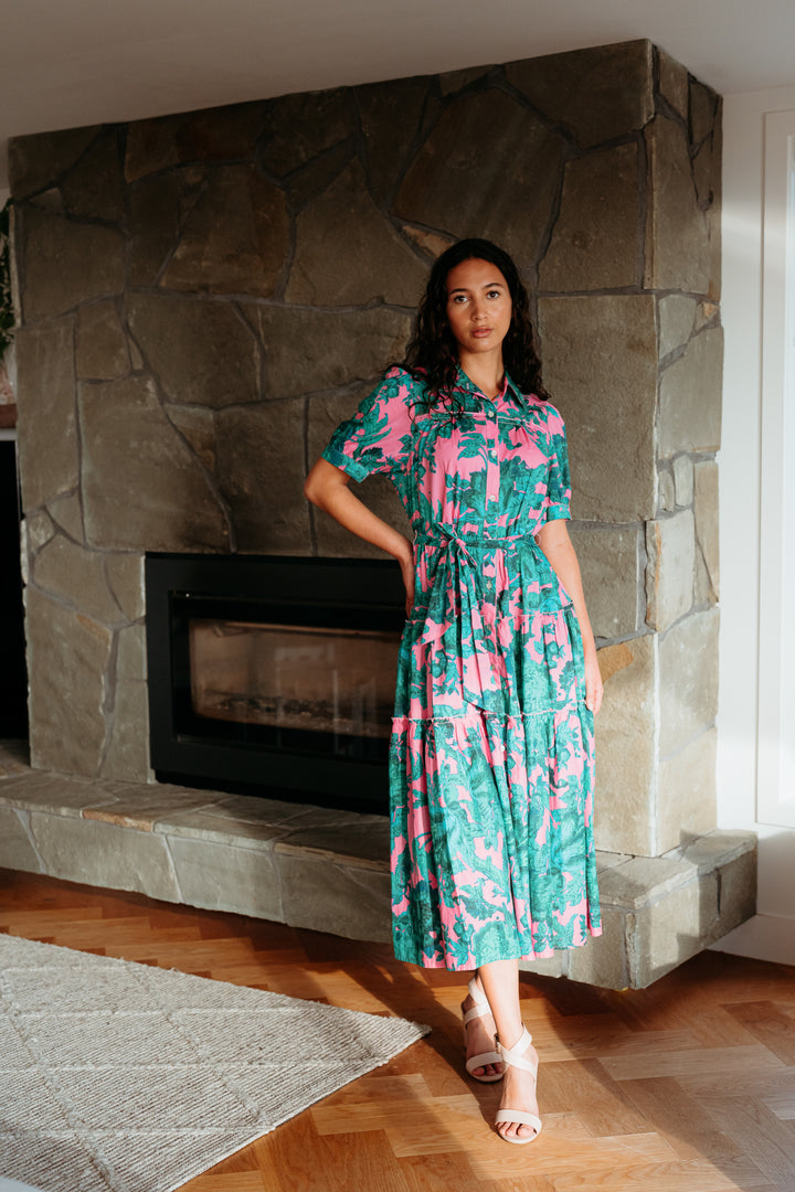 Woman in a floral dress standing in front of a stone fireplace.