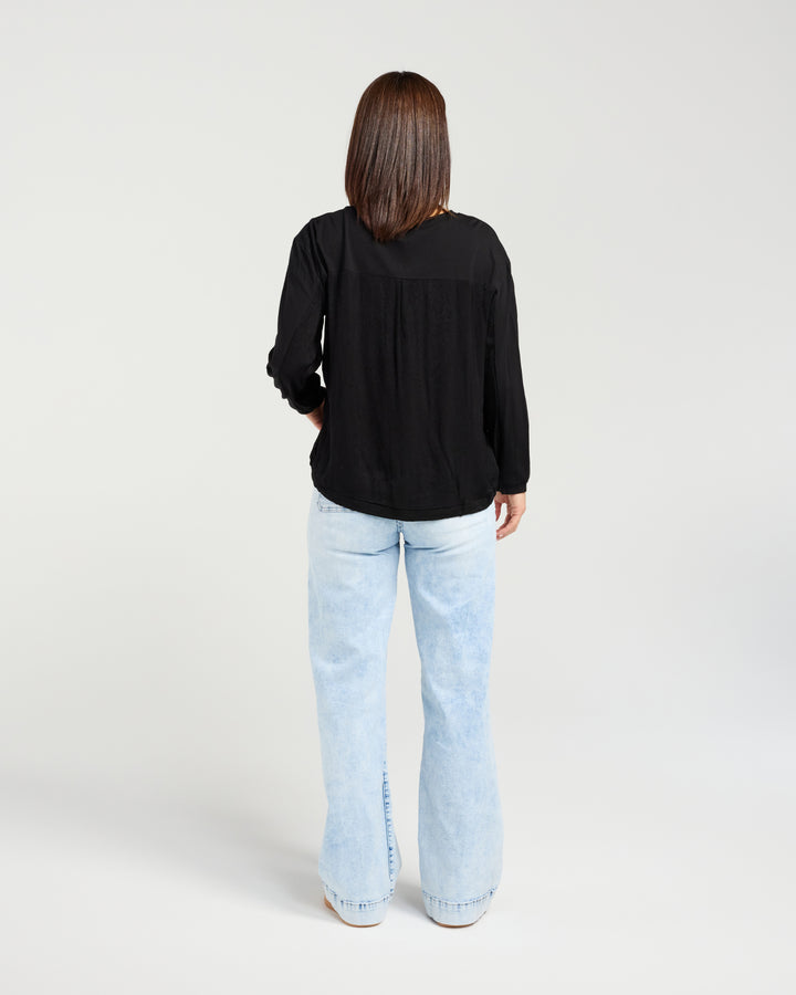 Person wearing a black long-sleeve top and light blue jeans on a white background
