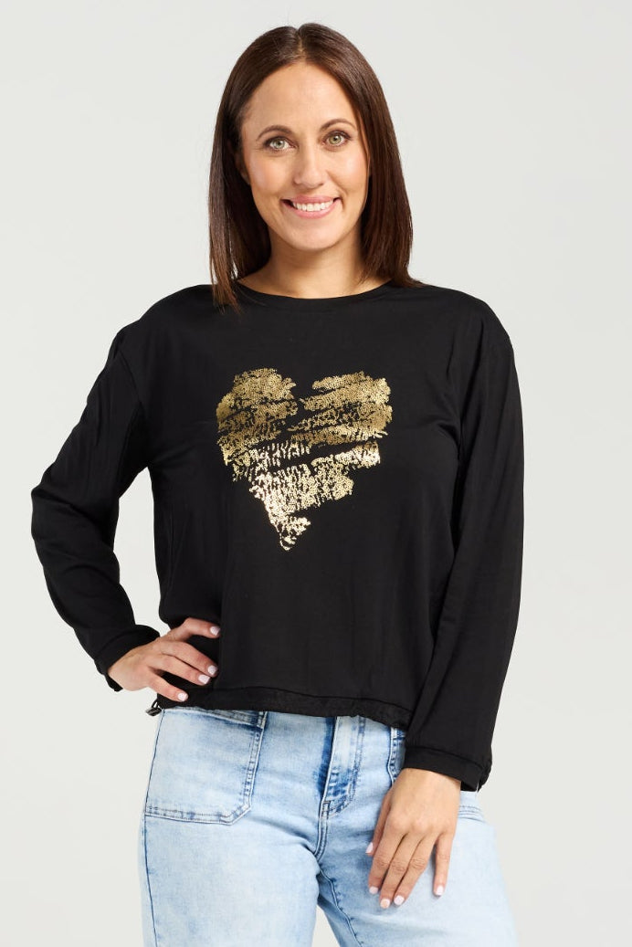 Woman wearing a black sweater with a gold heart design and light blue jeans on a white background