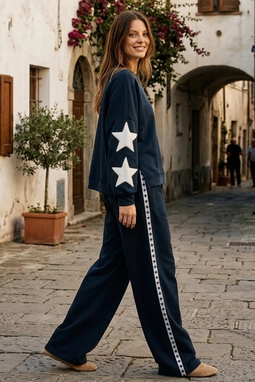 Woman in a navy blue outfit with white stars walking down a narrow street in an old town.