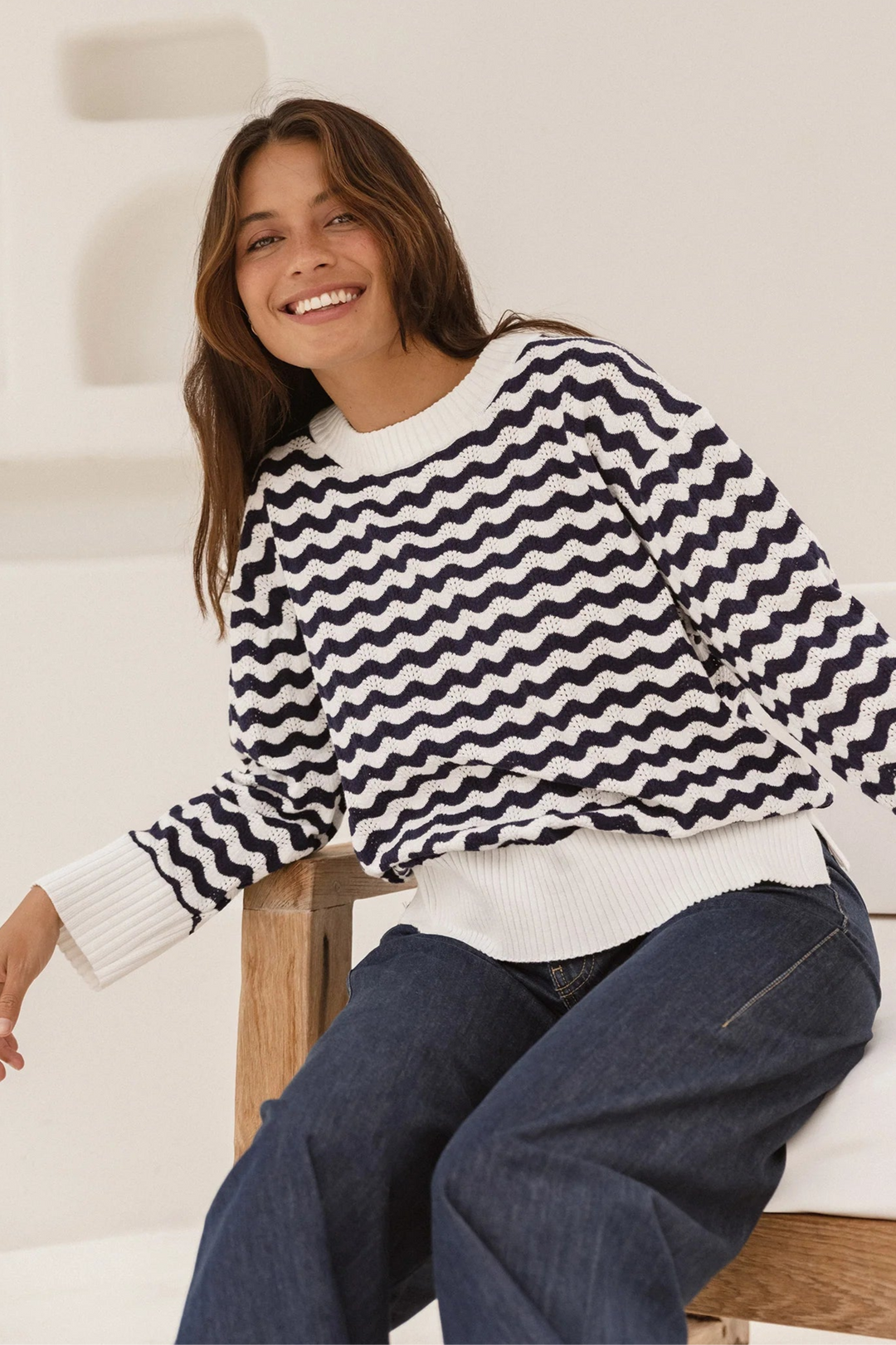 Woman wearing a black and white striped sweater sitting on a wooden stool.