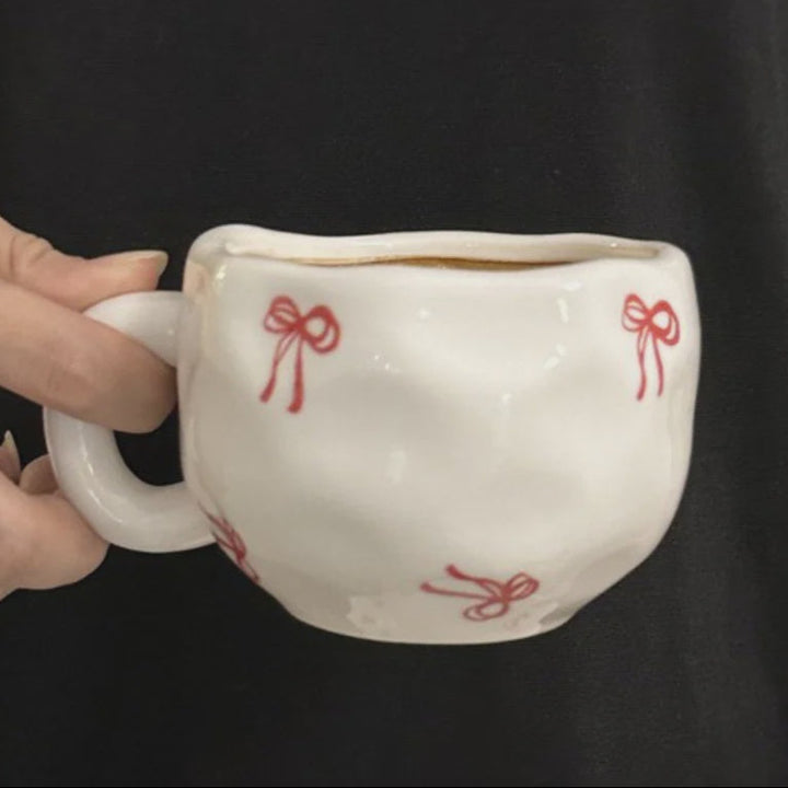 White ceramic cup with red bows held by a hand against a black background
