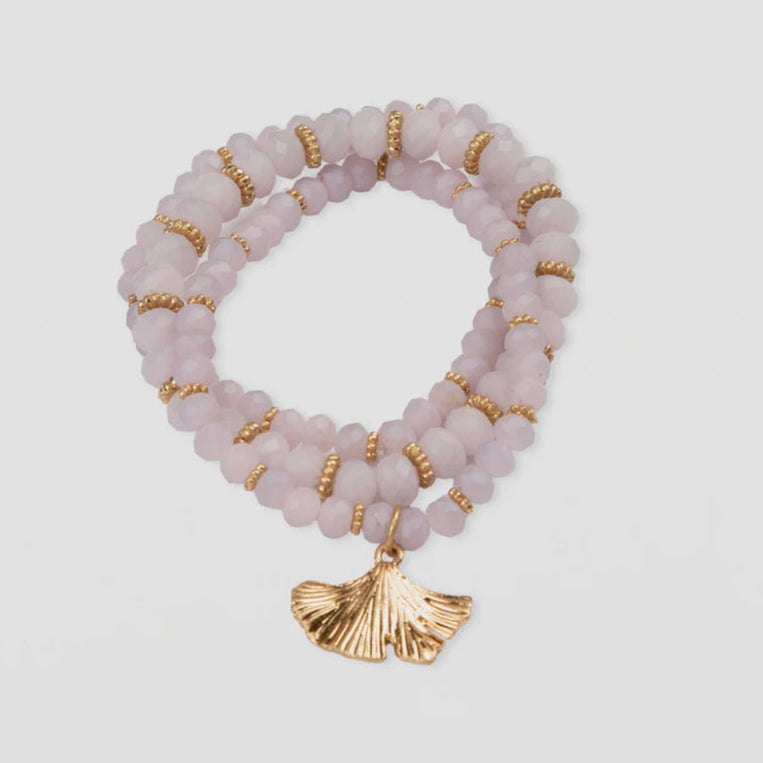 Beaded bracelet with gold accents and a shell charm on a light gray background