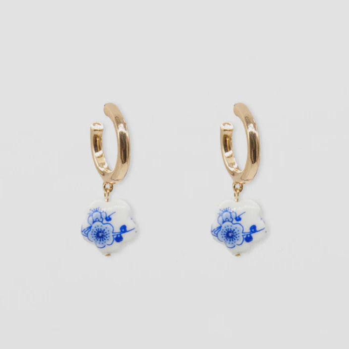 Pair of gold hoop earrings with blue floral designs on a light gray background