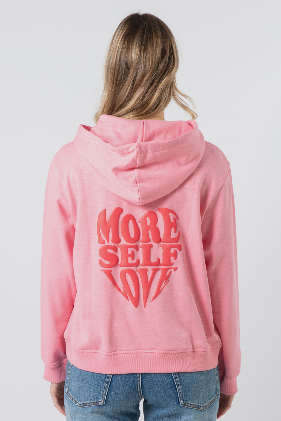 Person wearing a pink hoodie with 'More Self Love' text on the back against a white background