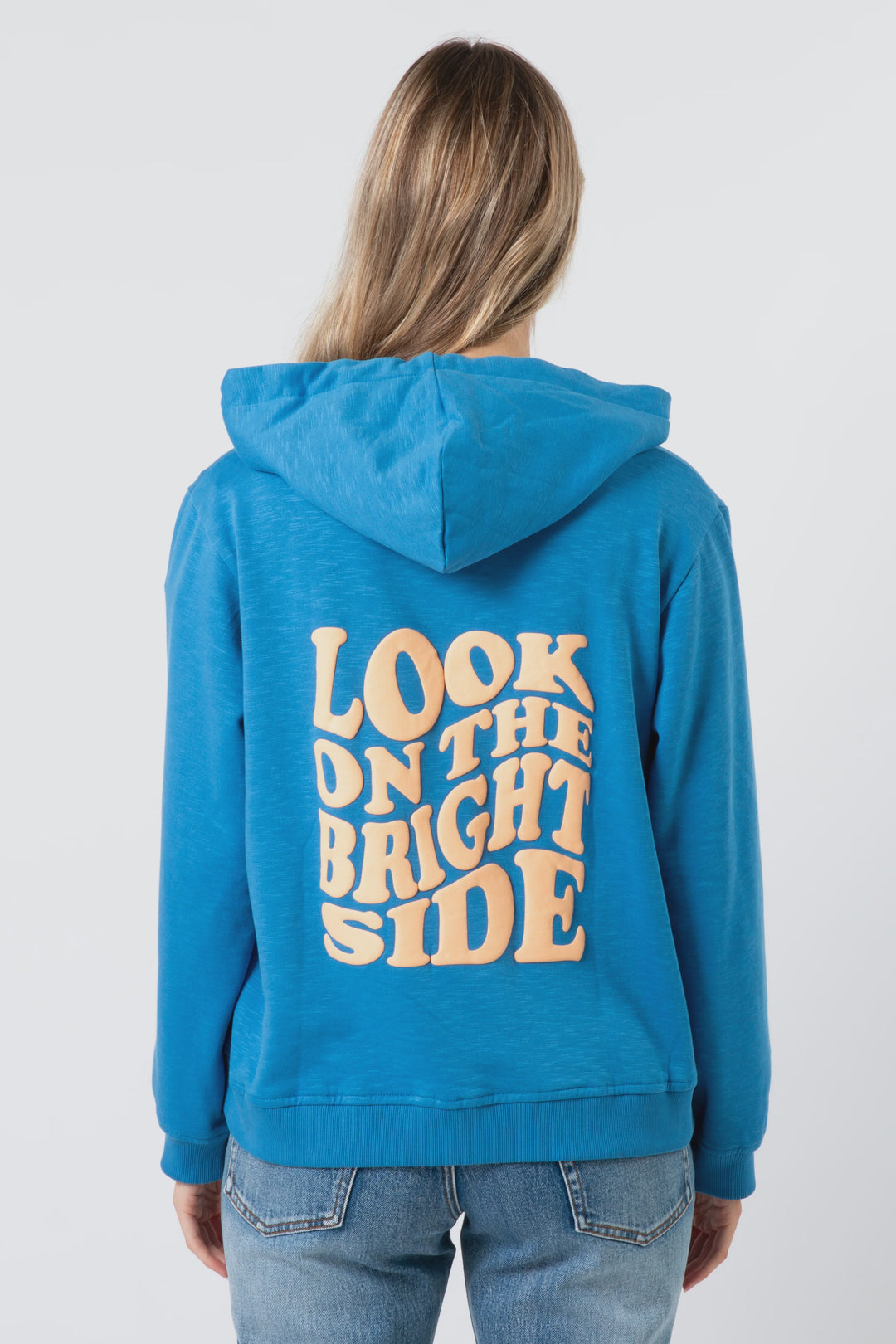 Person wearing a blue hoodie with 'Look on the bright side' text on the back against a plain background