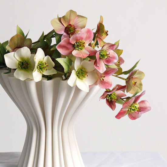 White vase with ribbed texture holding pink and white flowers on a white background