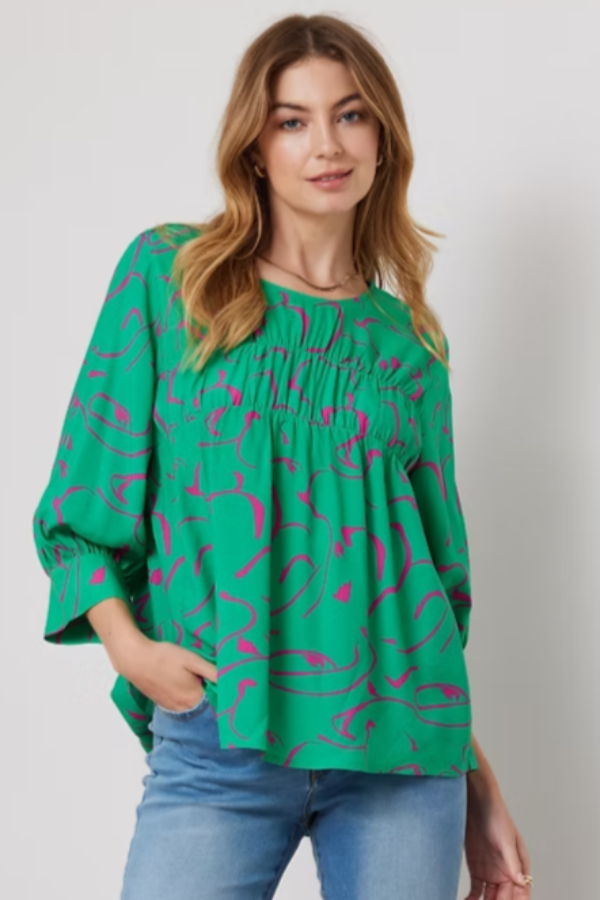Woman wearing a green blouse with pink patterns and blue jeans on a plain background