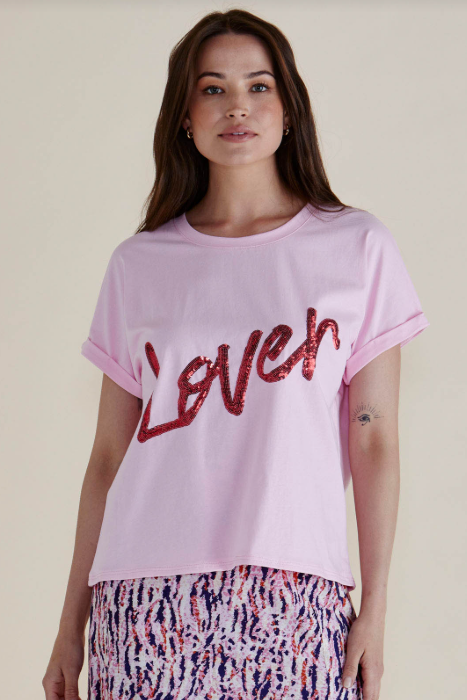Woman wearing a pink t-shirt with 'LOVE' printed in red sequins on a beige background