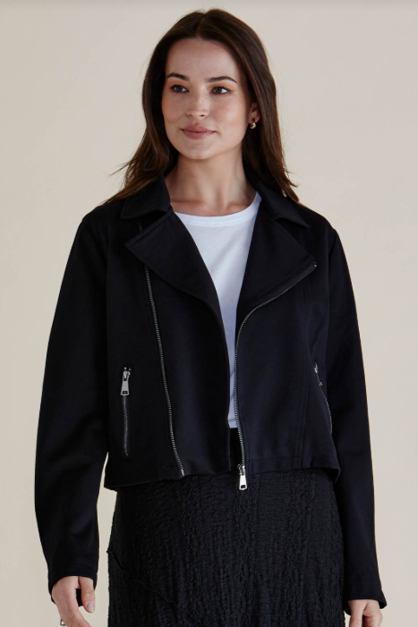 Woman wearing a black jacket over a white shirt on a beige background