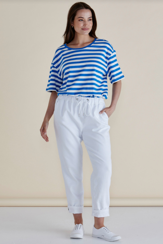 Woman wearing a blue and white striped shirt and white pants against a beige background