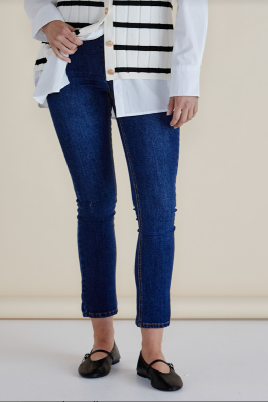 Person wearing blue jeans and a white sweater with black stripes on a beige background