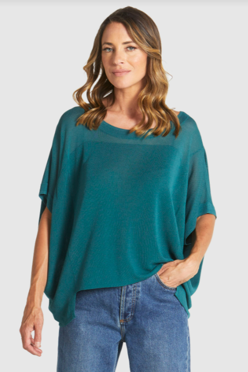 Woman wearing a teal poncho and blue jeans on a white background