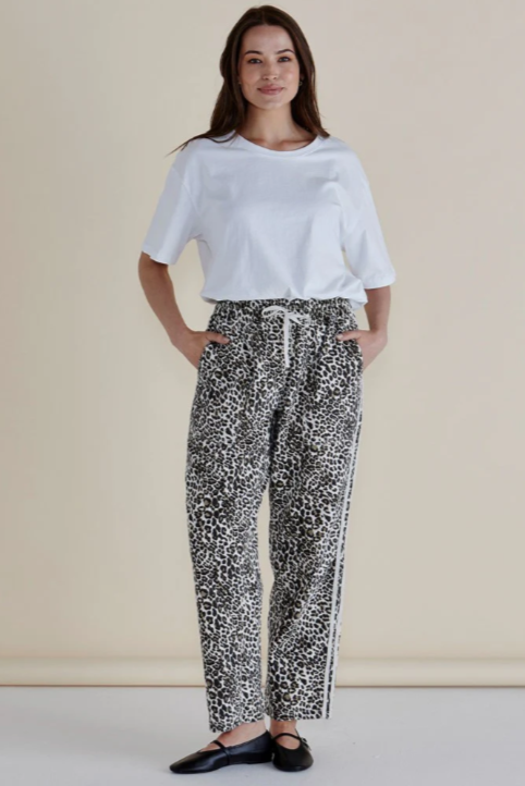 Woman wearing a white top and patterned pants against a beige background