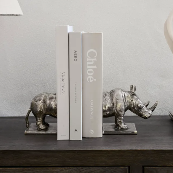 Decorative bookends shaped like rhinos on a shelf with books.