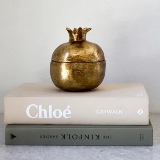 Gold pomegranate-shaped container on top of books with a plain background