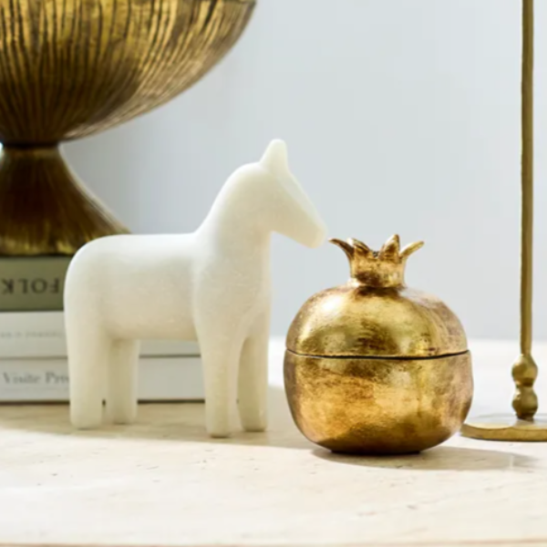Decorative items including a white horse figure and gold pomegranate-shaped box on a marble surface.