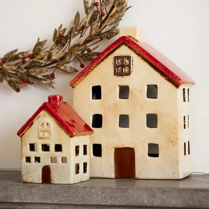 Two ceramic house-shaped candle holders with red roofs on a surface.
