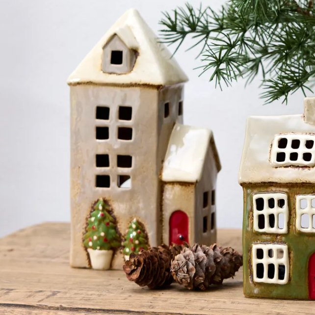 Set of ceramic houses with decorative trees and pinecones on a wooden surface.