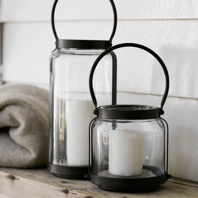 Two glass lanterns with black metal handles on a wooden surface.